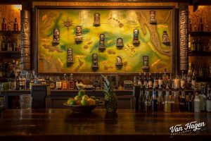 Image of the back bar from Latitude 29 (New Orleans) shows a large map populated with tiki mugs of various regions